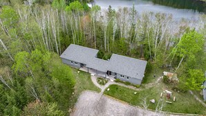 Eine Luftaufnahme eines zweistöckigen Hauses mit einer großen Terrasse, umgeben von dichtem Wald und einem See.