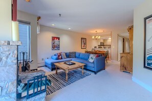 A living room with a blue sofa, a wooden coffee table, and a stone fireplace. - Stratton walk on/ski off, King bed, walk 2 food/drink (Stratton)