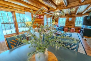 A log cabin interior with a dining area, a sofa, and a sign indicating a ski lift nearby. - Stratton; 4 min. Renovated, games, fireplace! (Jamaica)