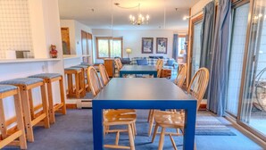 A dining area with a long table and wooden chairs, a chandelier, and a view through a glass door. - Stratton walk on/off, walk to food/drink, fireplace (Stratton)