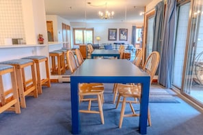 A dining area with a long table and wooden chairs, a chandelier, and a view through a glass door. - Stratton walk on/off, walk to food/drink, fireplace (Stratton)