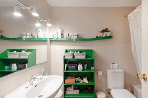 Une salle de bain équipée d’un lavabo, de toilettes et d’étagères où sont rangés les produits de toilette.