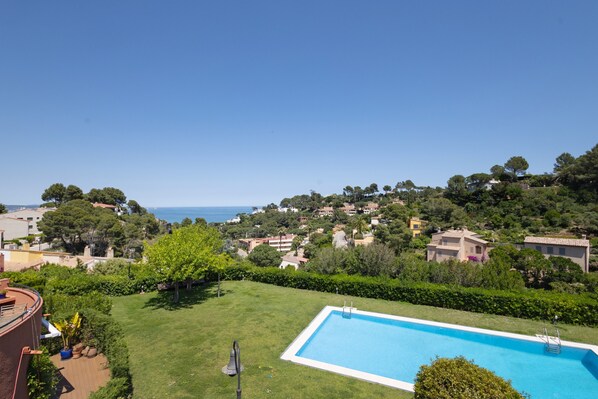 Une piscine offrant une vue dégagée sur la mer, entourée d’une végétation luxuriante et de bâtiments résidentiels.