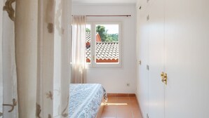Un pasillo estrecho con una cama, un ventanal con vista a un tejado de tejas y una puerta con pomo.