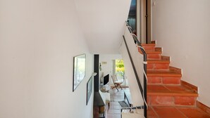 Una escalera con peldaños rojos que lleva a un rellano con un televisor, una silla y una ventana.