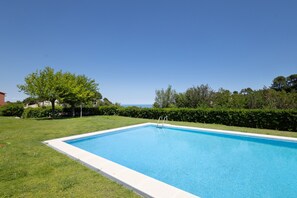 Une piscine rectangulaire bordée de blanc, entourée d’une pelouse bien entretenue et d’une haie.