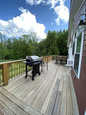 A wooden deck with a grill and outdoor furniture, overlooking a forested area. - Bromley; 7 min. XC skiing! 7 acres. Pond. Dogs OK. (Peru)
