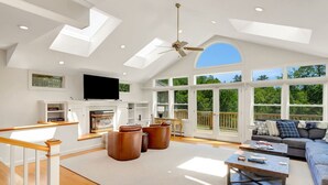 Un salón amplio con techo alto, tragaluces, chimenea y ventanas grandes que ofrecen vistas al exterior.