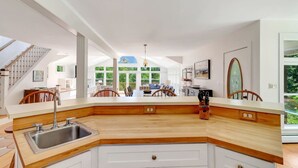 Cocina moderna con encimera de madera, armarios blancos y un ventanal con vistas a zonas verdes.