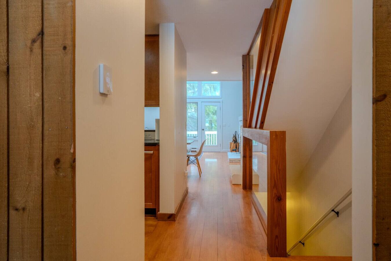 Un pasillo con suelo de madera, una escalera y vistas a una habitación con ventana.