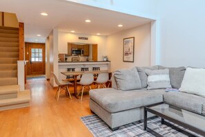 A modern living room with a grey sectional sofa, a coffee table, and a dining area with a wooden table and chairs. - POOL! Ski/walk on/off, King beds, Hot Tub (Stratton)