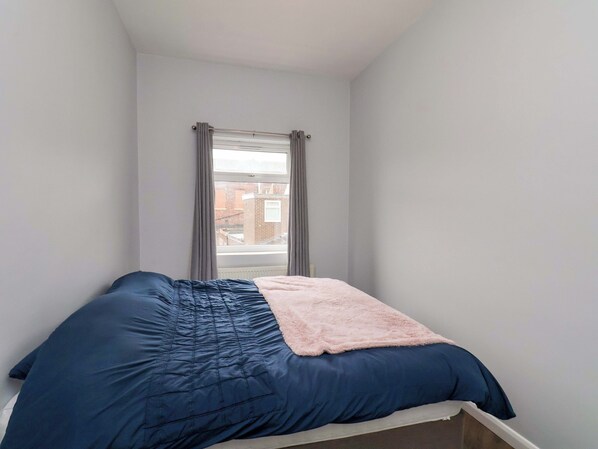 A bedroom with a bed, a window with curtains, and a view of buildings outside.