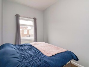 Un dormitorio con una cama, un ventanal con cortinas y vista a un edificio de ladrillo.