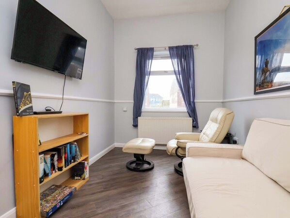 A room with a sofa, a chair, a bookshelf, a flat-screen TV, a window with curtains, and a radiator. - Bartletts Base (Stockton-on-Tees)
