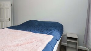 Une chambre à coucher avec un lit, une porte blanche, une table de chevet blanche et un rideau de couleur claire.