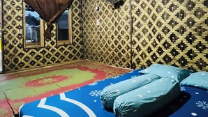 Een kamer met een behang, een bed met blauw beddengoed, een raam met gordijn en een plafondventilator.