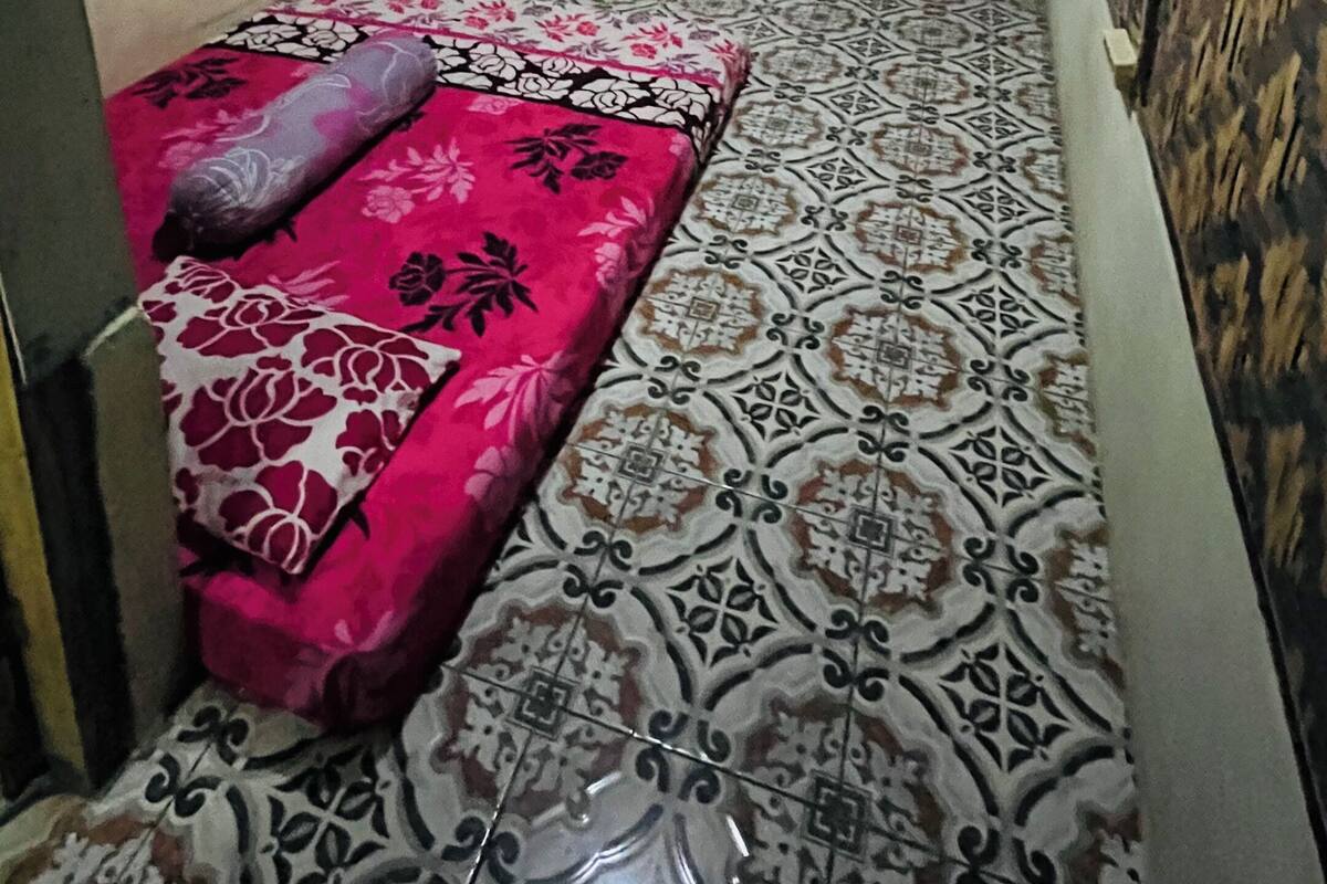 A small room with a bed, a window with a curtain, a door, and patterned walls.
