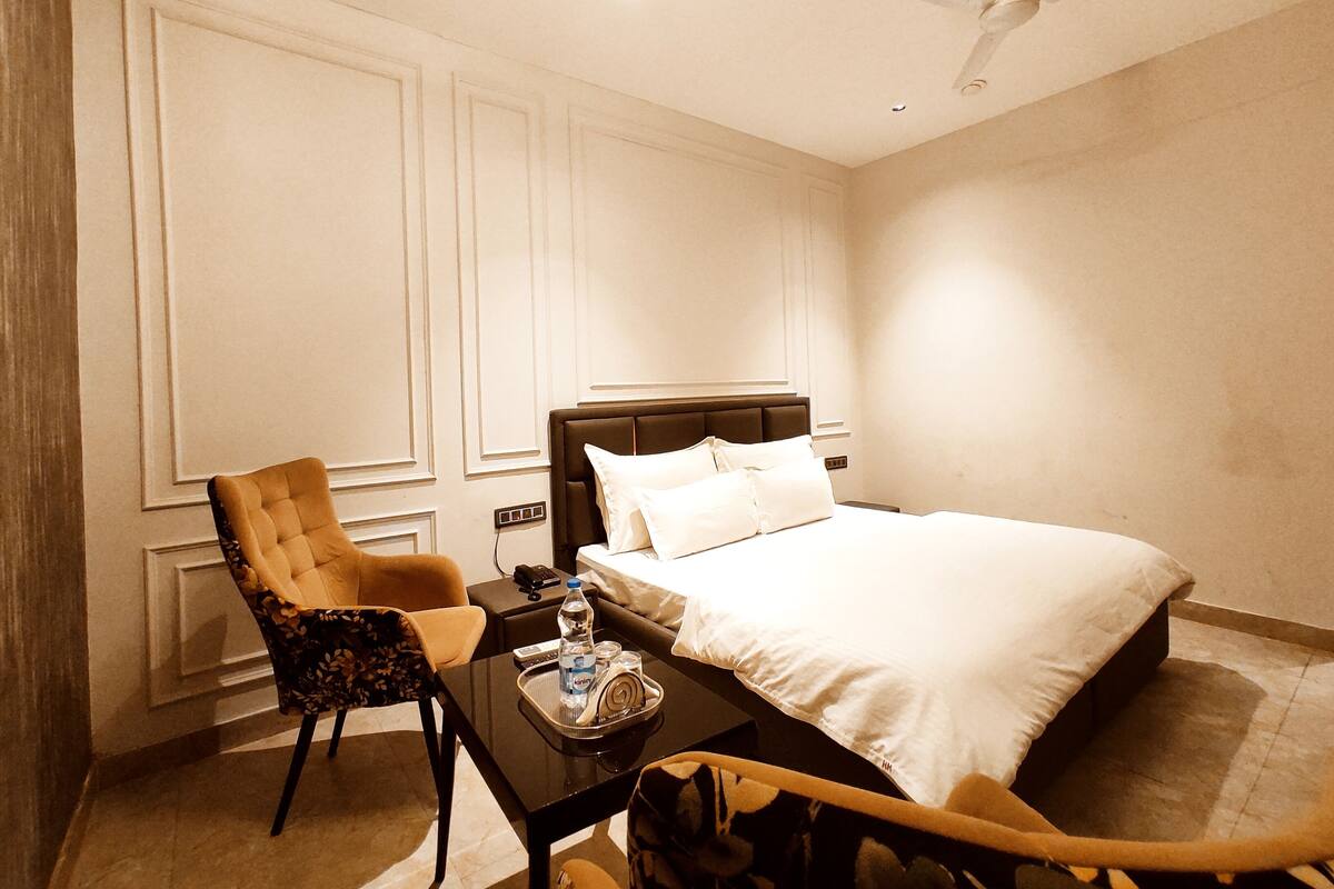 A hotel room with a bed, a chair, a table with a tray, and a ceiling fan.