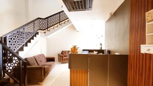 En receptionsdisk, en trappe med dekorativ gelænder og en brun sofa i en moderne lobby.