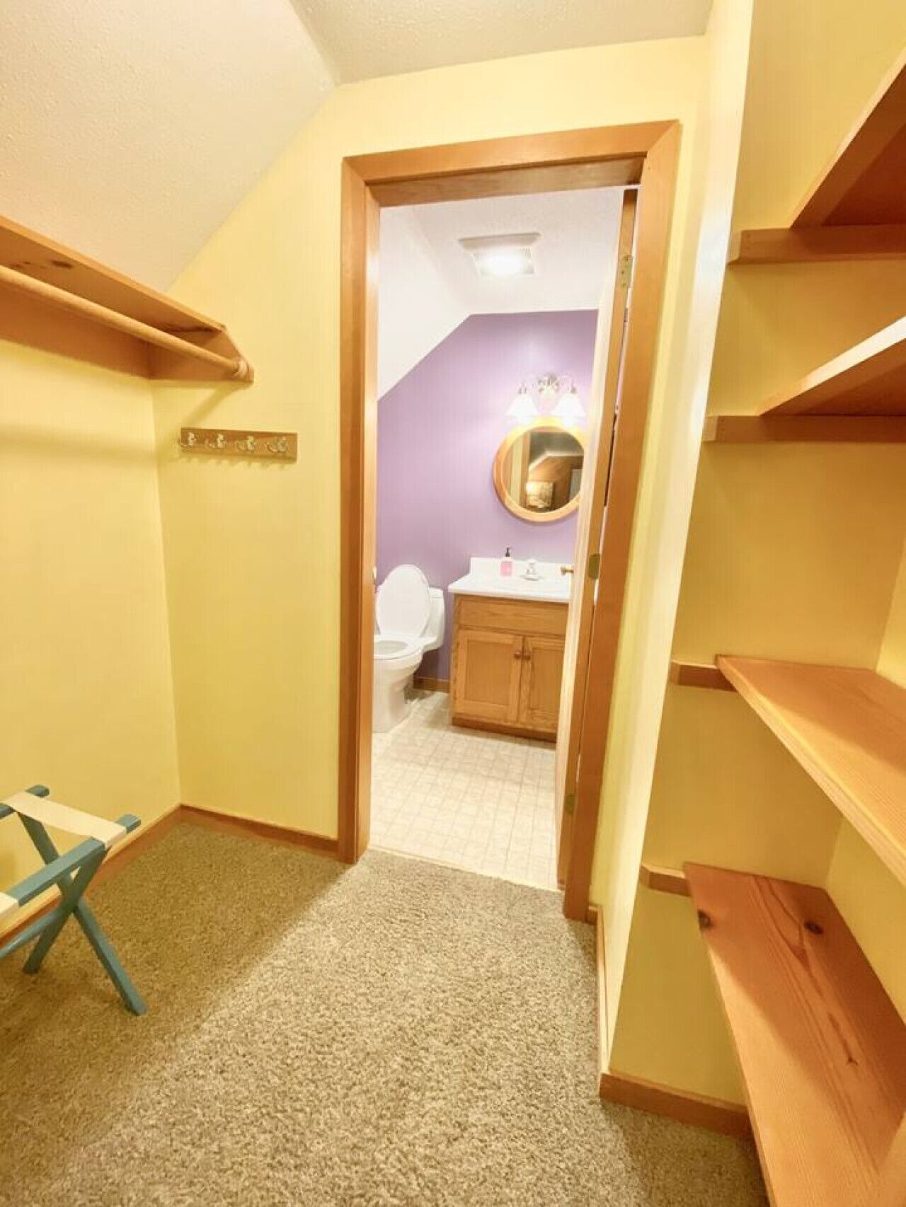 A narrow hallway with a wooden bench, a small table, and a door leading to a bathroom with a toilet and a sink.