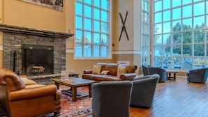 A spacious living room with a stone fireplace, large windows, and a view of the outdoors.