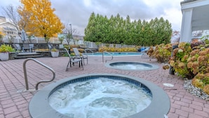 A spa area with two hot tubs, lounge chairs, and a pool.