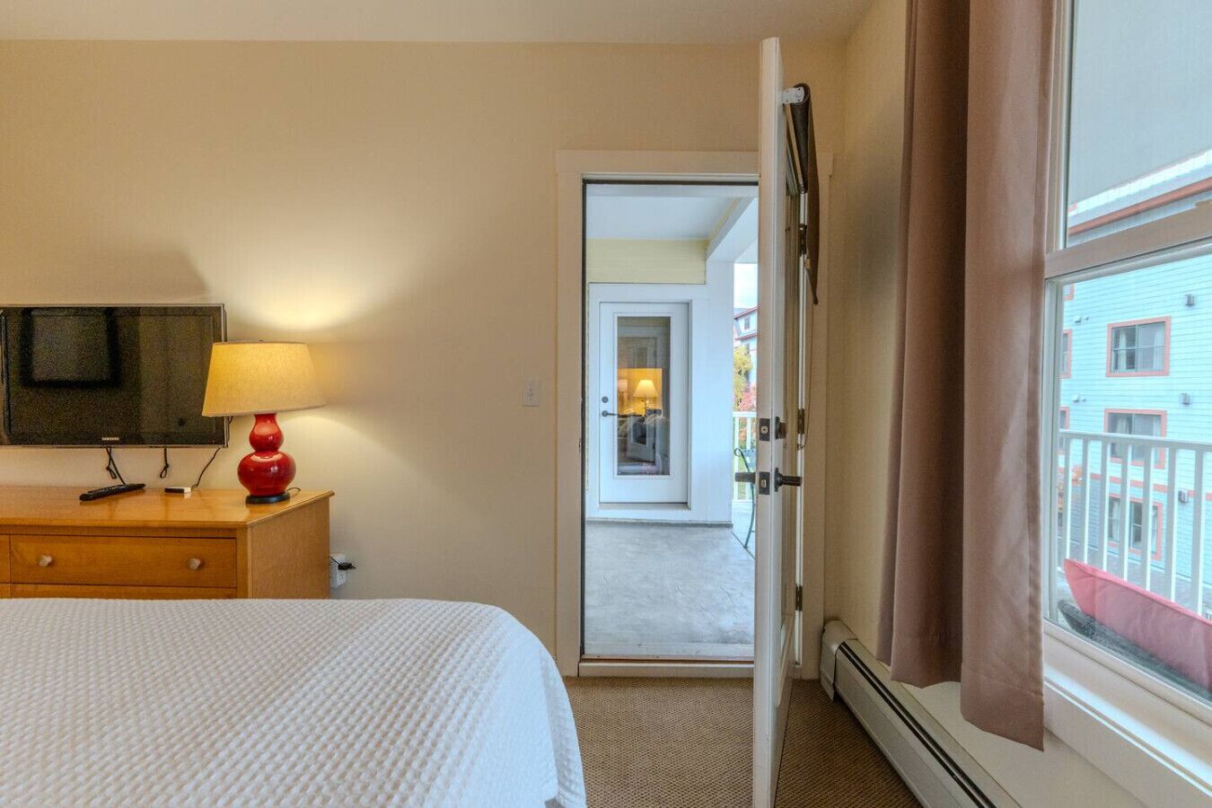 A hotel room with a bed, a TV, a lamp, and a view of the outside balcony.