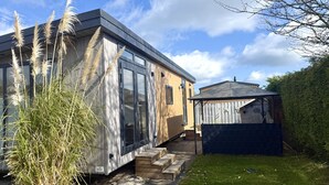 Ein modernes Haus mit großen Fenstern, einer Holzdiele und einem kleinen Geräteschuppen.