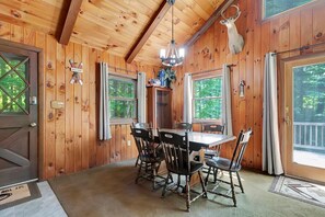 Ein Holzblockhaus-Interieur mit Esstisch, Stühlen, einer Chandelieber und einem an der Wand befestigten Hirschkopf.
