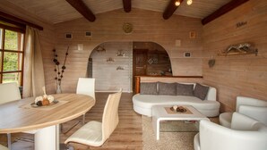 Un'atmosfera accogliente con soffitto in legno, un tavolo da pranzo rotondo, divani bianchi e una zona cucina visibile attraverso un arco.