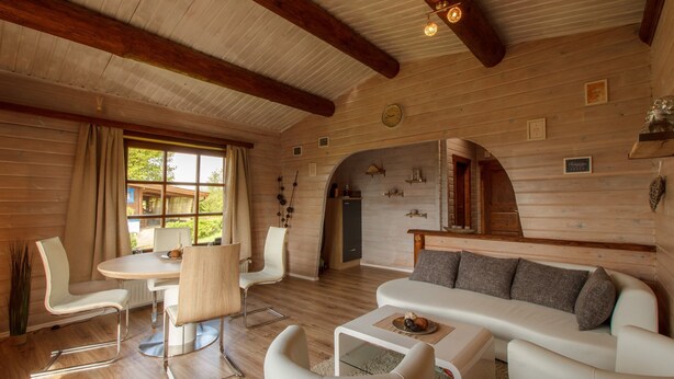 Interno di una baita in legno con zona pranzo, divano e camino.