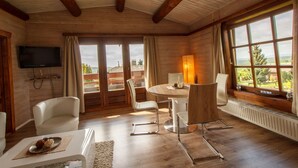 Una stanza con soffitto in legno, una TV a parete, un tavolo da pranzo con sedie e una finestra vista all'esterno.