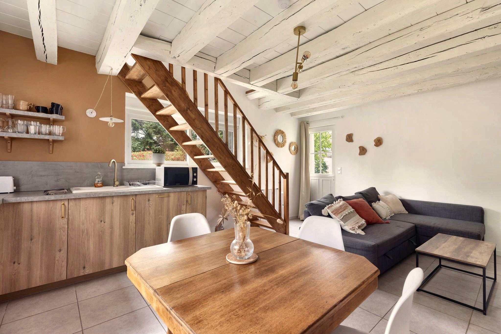 Eine moderne Küche mit einer Holztreppe, einem Essbereich mit einem Holztisch und einem Wohnzimmer mit Sofa und Couchtisch.