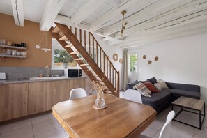 A modern kitchen with a wooden staircase, a dining area with a wooden table, and a living room with a sofa. - Chez Cocotte 4 guests with heated pool from mid-May to September (Veuzain-sur-Loire)