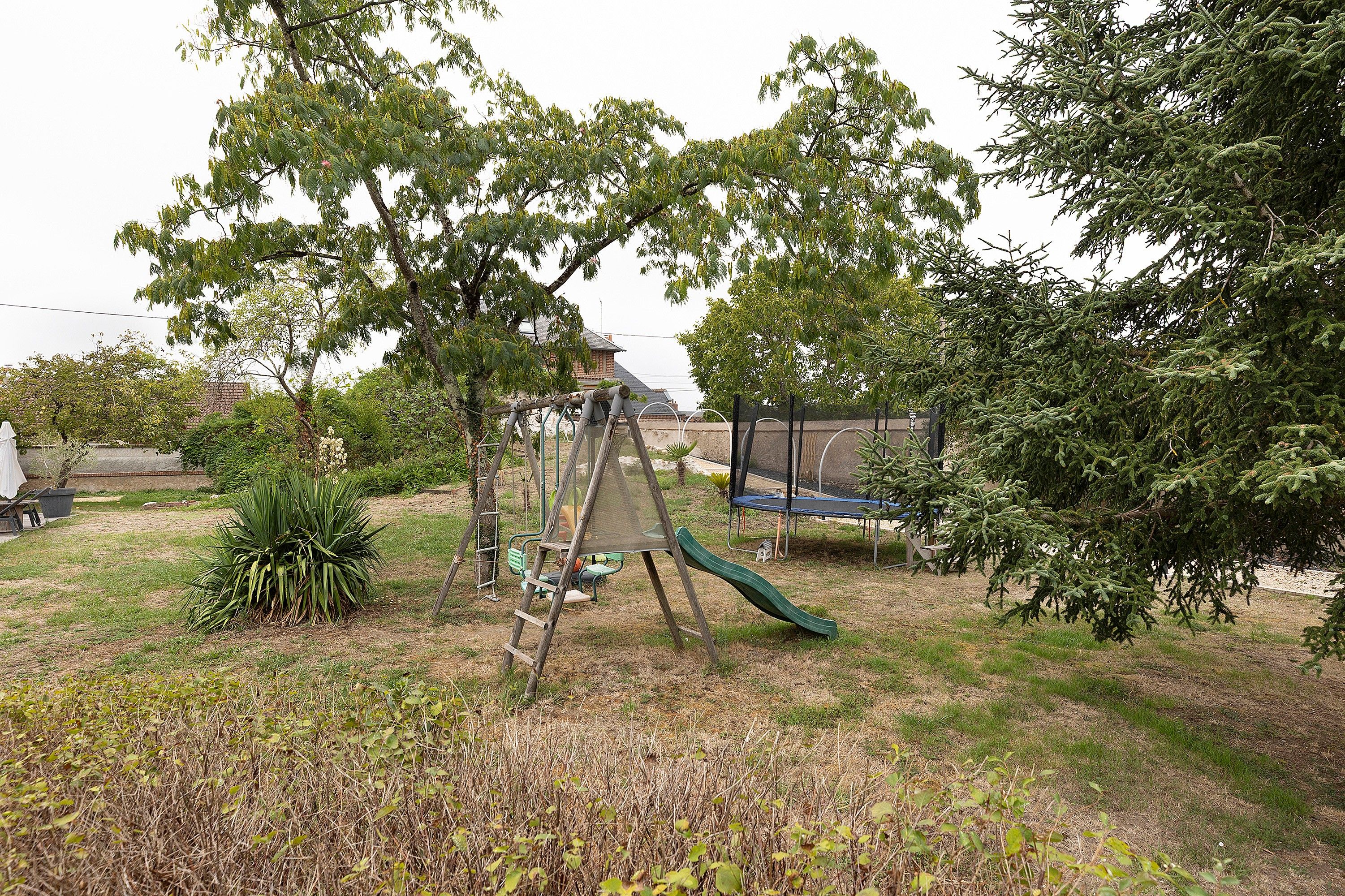 A backyard with a swing set, a trampoline, and a small garden area.
