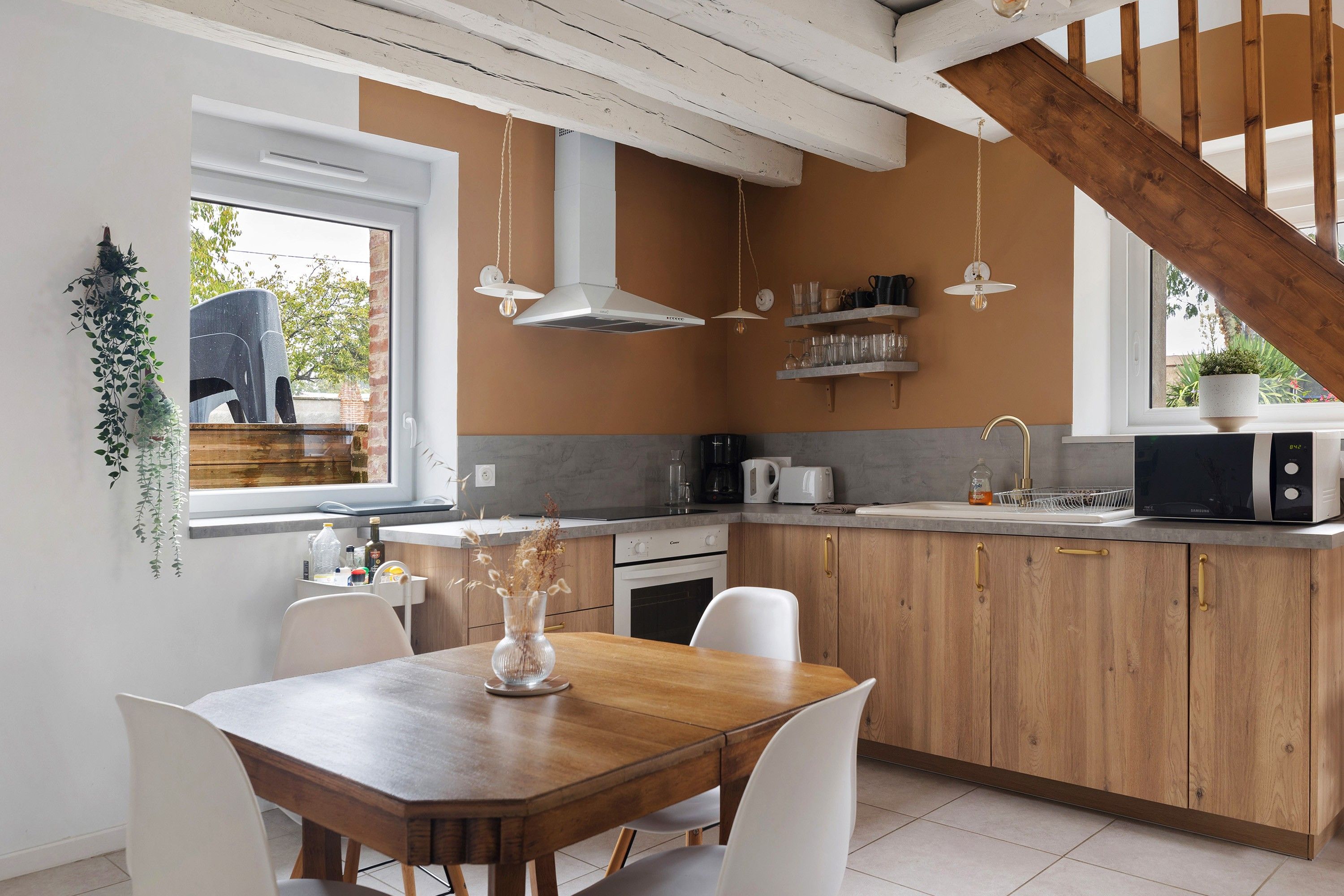 A modern kitchen with wooden cabinets, a dining table, and a hanging light fixture.