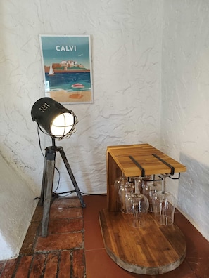 A rustic room with a wooden table holding wine glasses, a vintage lamp, and a poster on the wall.