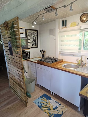 A kitchen with a wooden countertop, a sink, a stove, and a dishwasher. There is a window with blinds, a clock, and a framed picture on the wall.