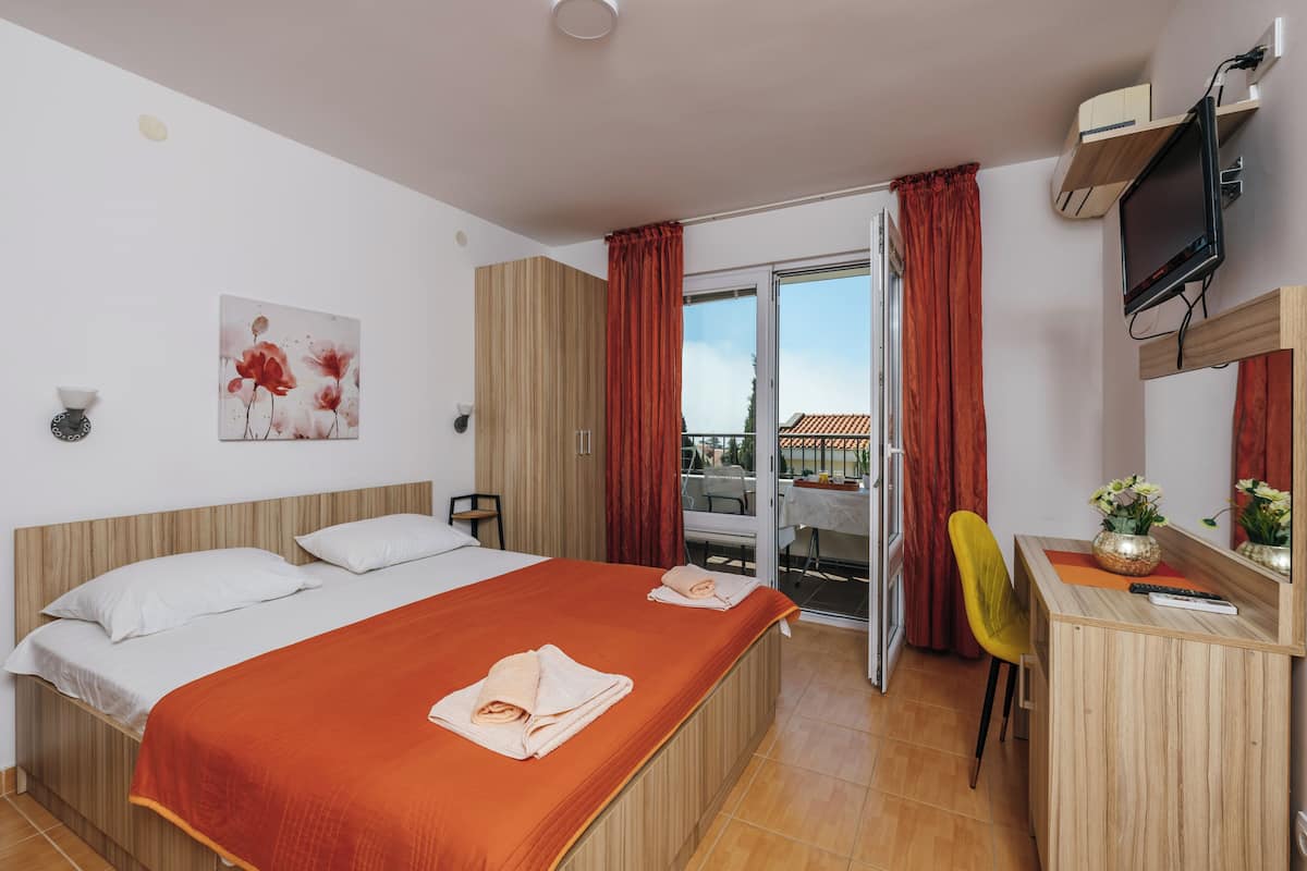 Habitación de hotel con cama, escritorio, silla, televisor y balcón con cortinas rojas.