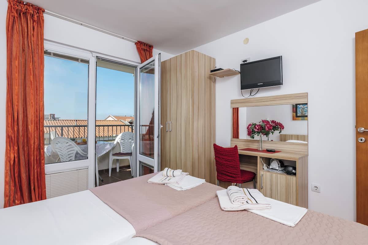 Habitación de hotel con cama, escritorio con silla, televisor y balcón con mesa y sillas.