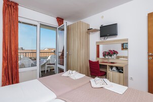 A hotel room with a bed, a desk with a chair, a television, and a balcony with a table and chairs.