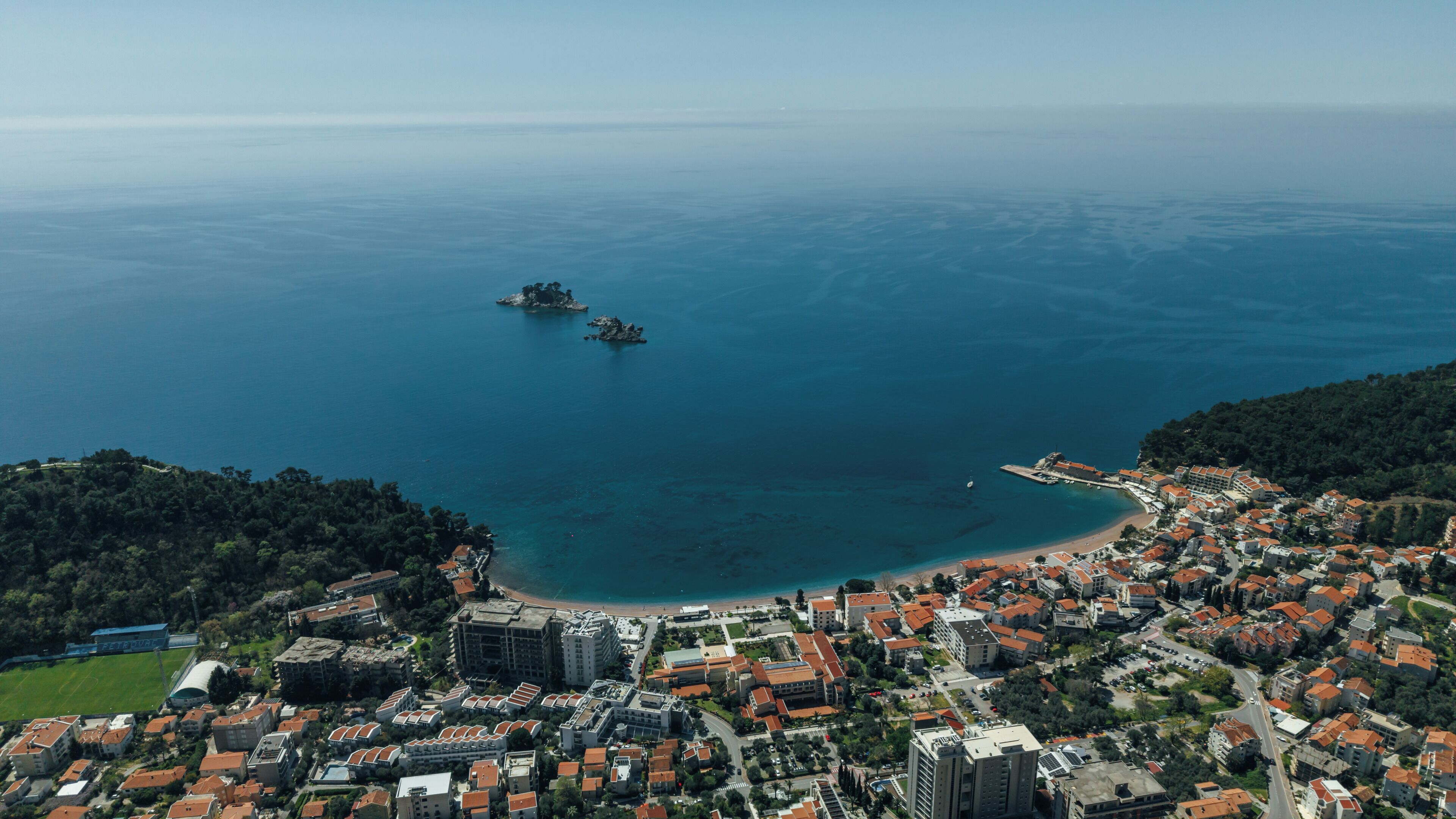 An aerial view of a coastal town with a beach, buildings, and a small island.