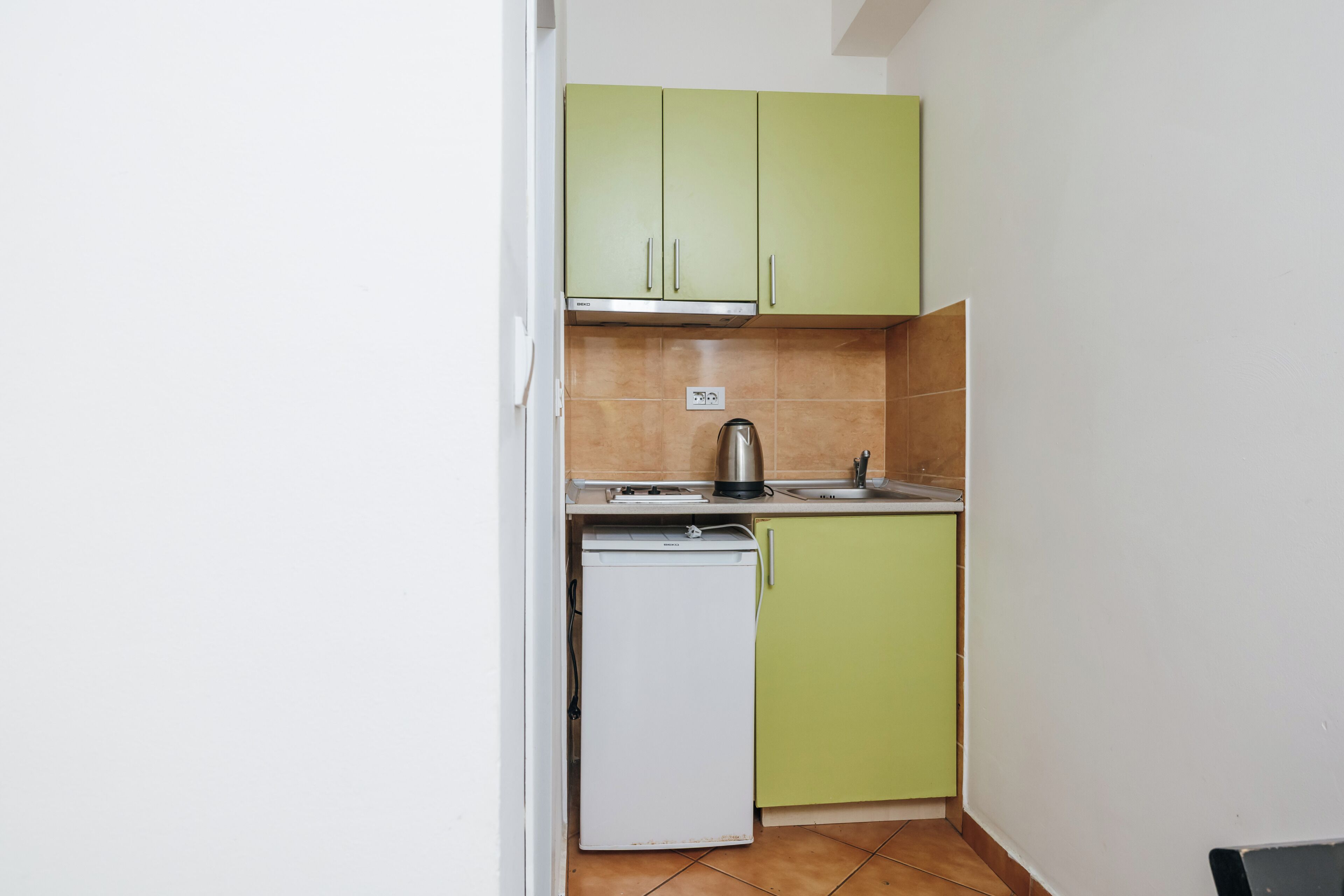 Una cocina compacta con armarios verdes, un lavavajillas blanco y un hervidor de acero inoxidable.