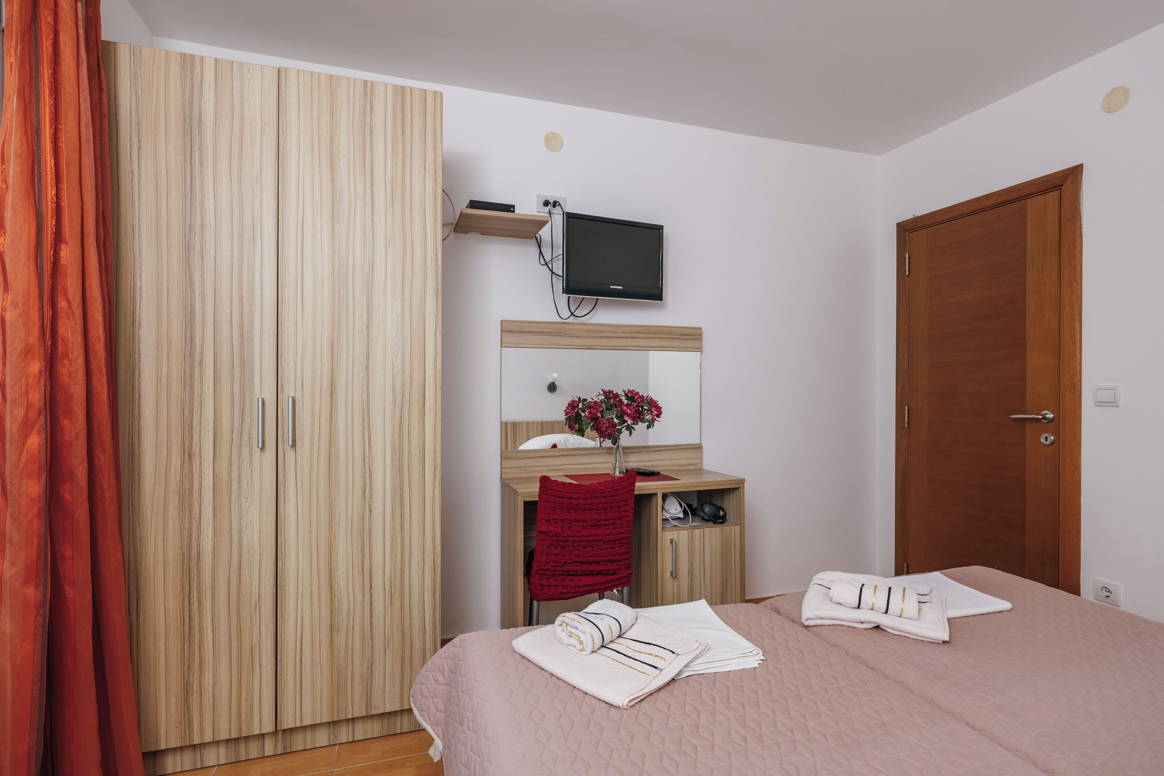 Une chambre à coucher avec un lit, une armoire, un bureau avec une télévision et une porte.
