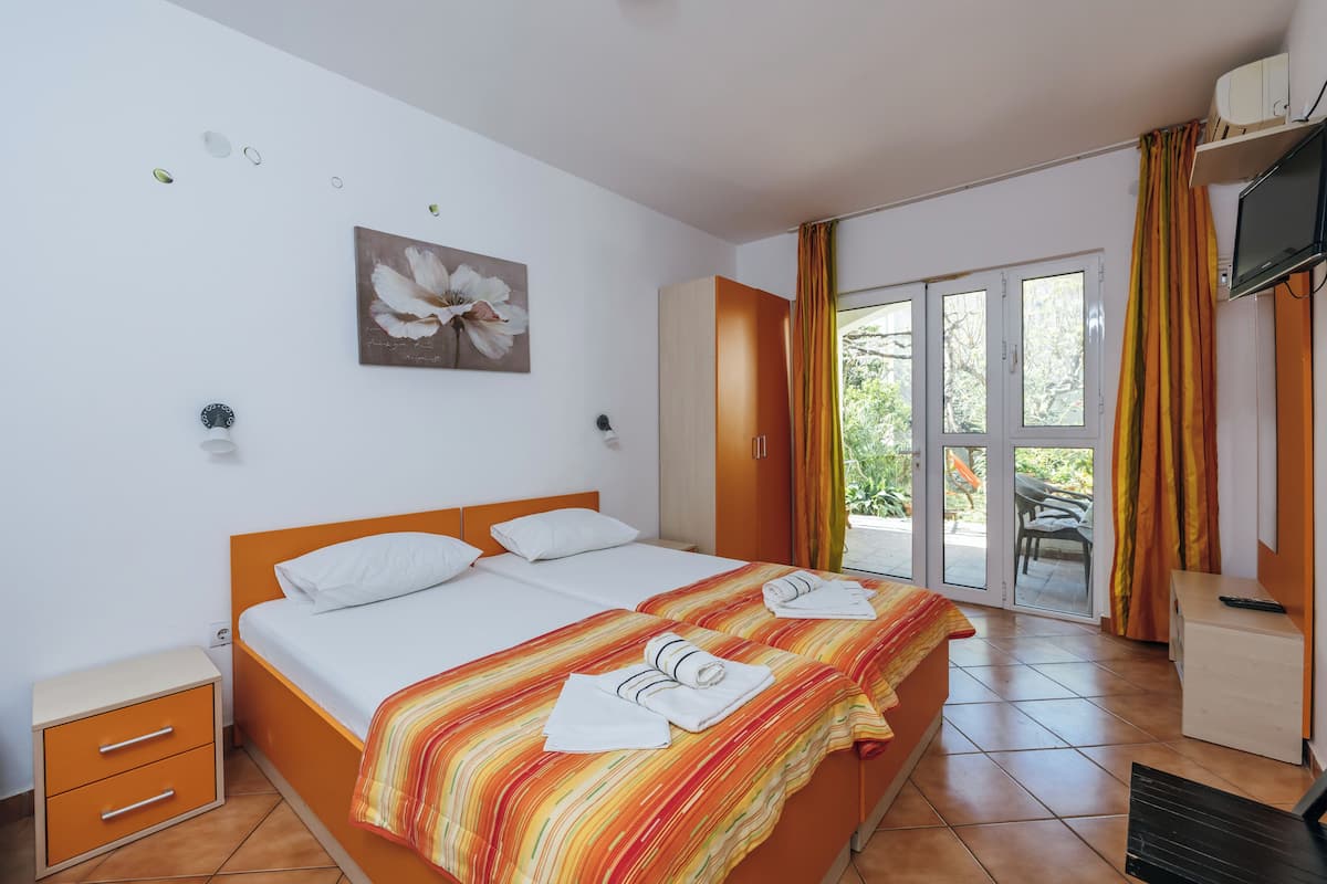Habitación de hotel con cama, mesita de noche, televisor y puerta corrediza de vidrio que da a un espacio exterior.