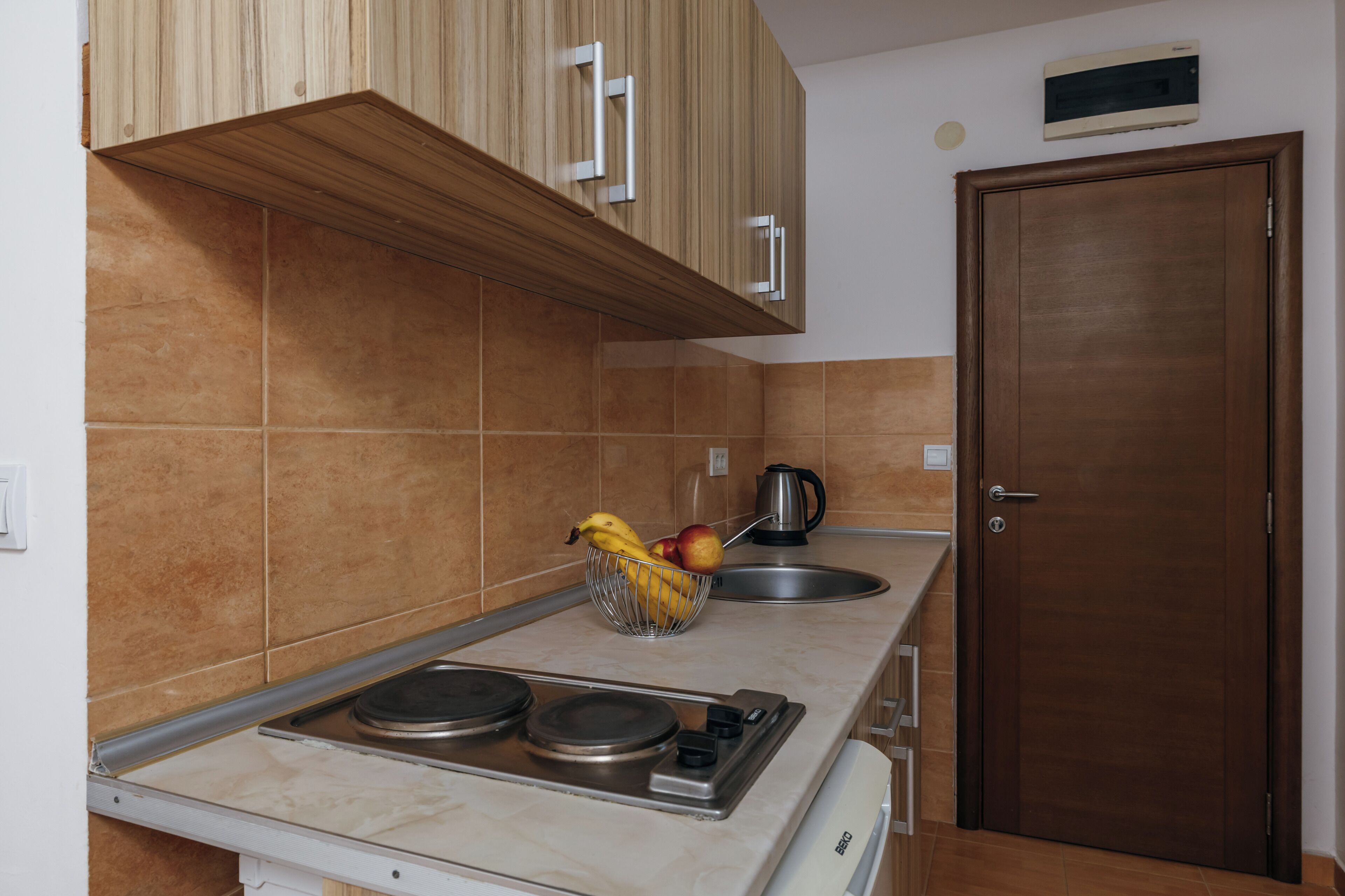 A kitchen with a stove, a sink, and a fruit bowl on the counter.