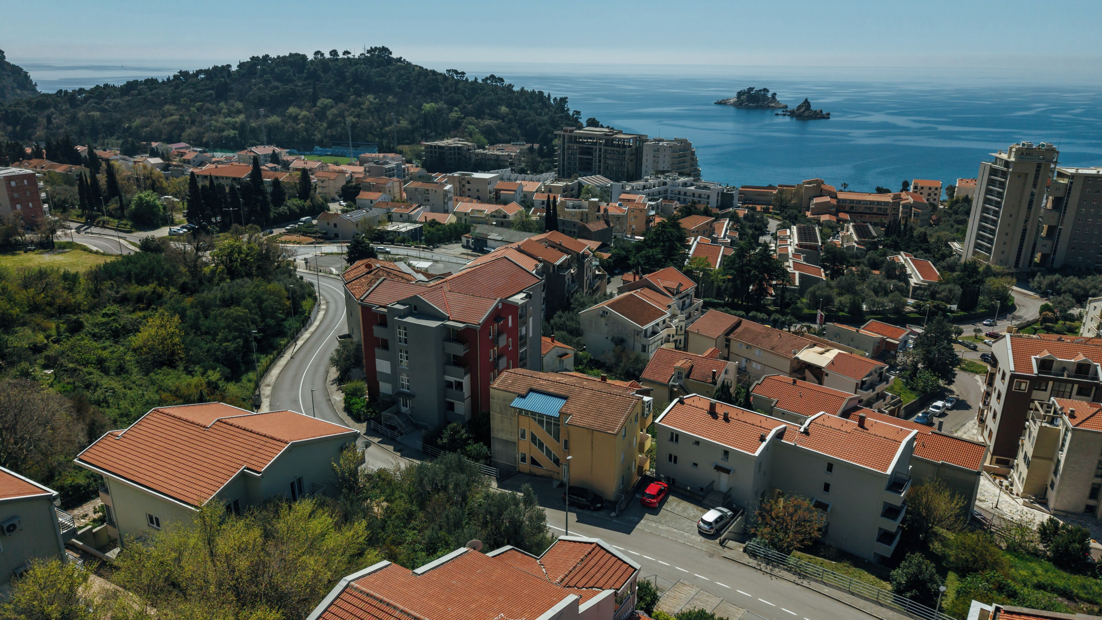 A coastal town with terracotta-roofed buildings, a winding road, and a view of the sea.