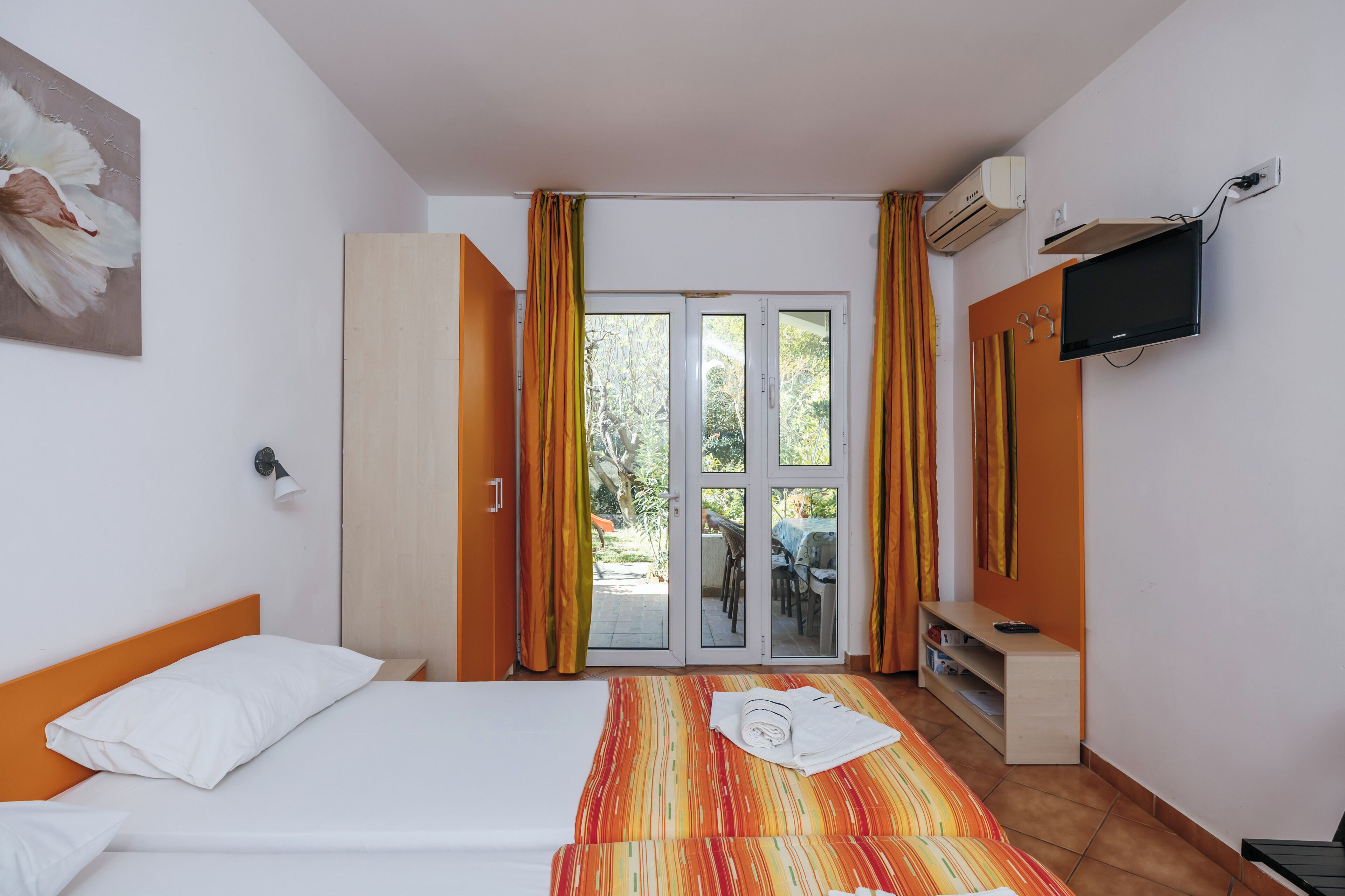 A hotel room with a bed, a TV, a wardrobe, and a sliding glass door leading to an outdoor area.