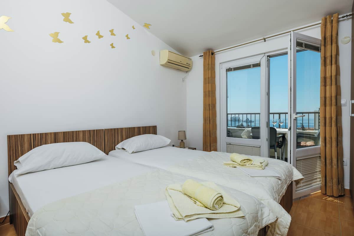 Habitación de hotel con dos camas, un balcón y vistas, y aire acondicionado.