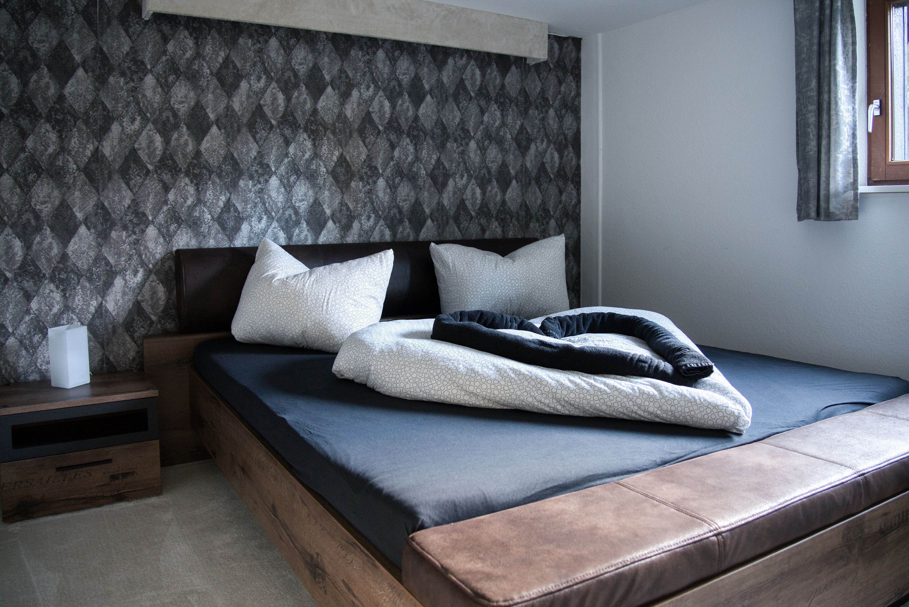 A bedroom with a bed, pillows, a nightstand, and a window with curtains.